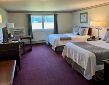 spacious room with purple carpet with two Queen beds each with cream comforters.