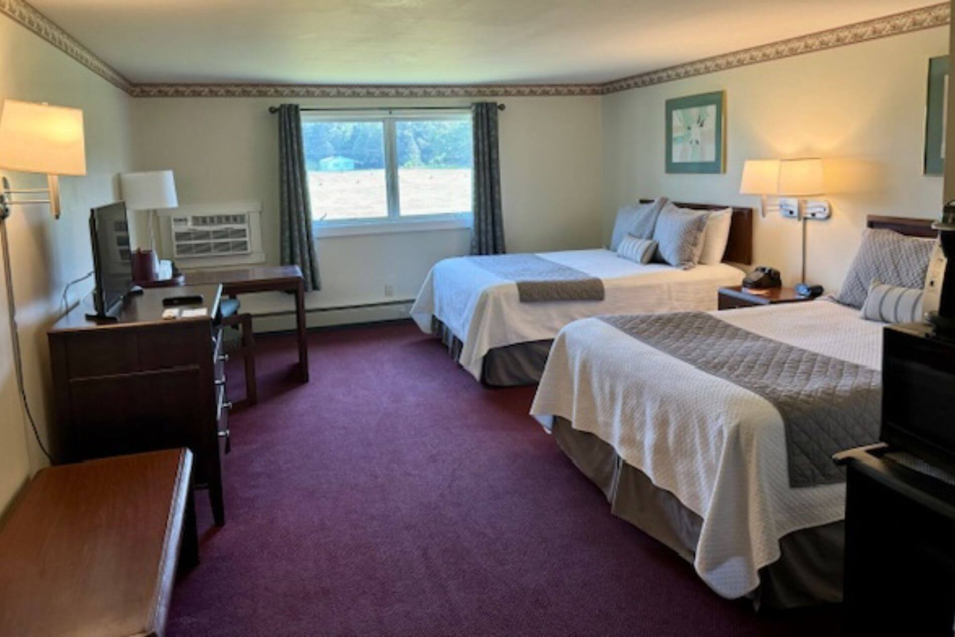 spacious room with purple carpet with two Queen beds each with cream comforters.