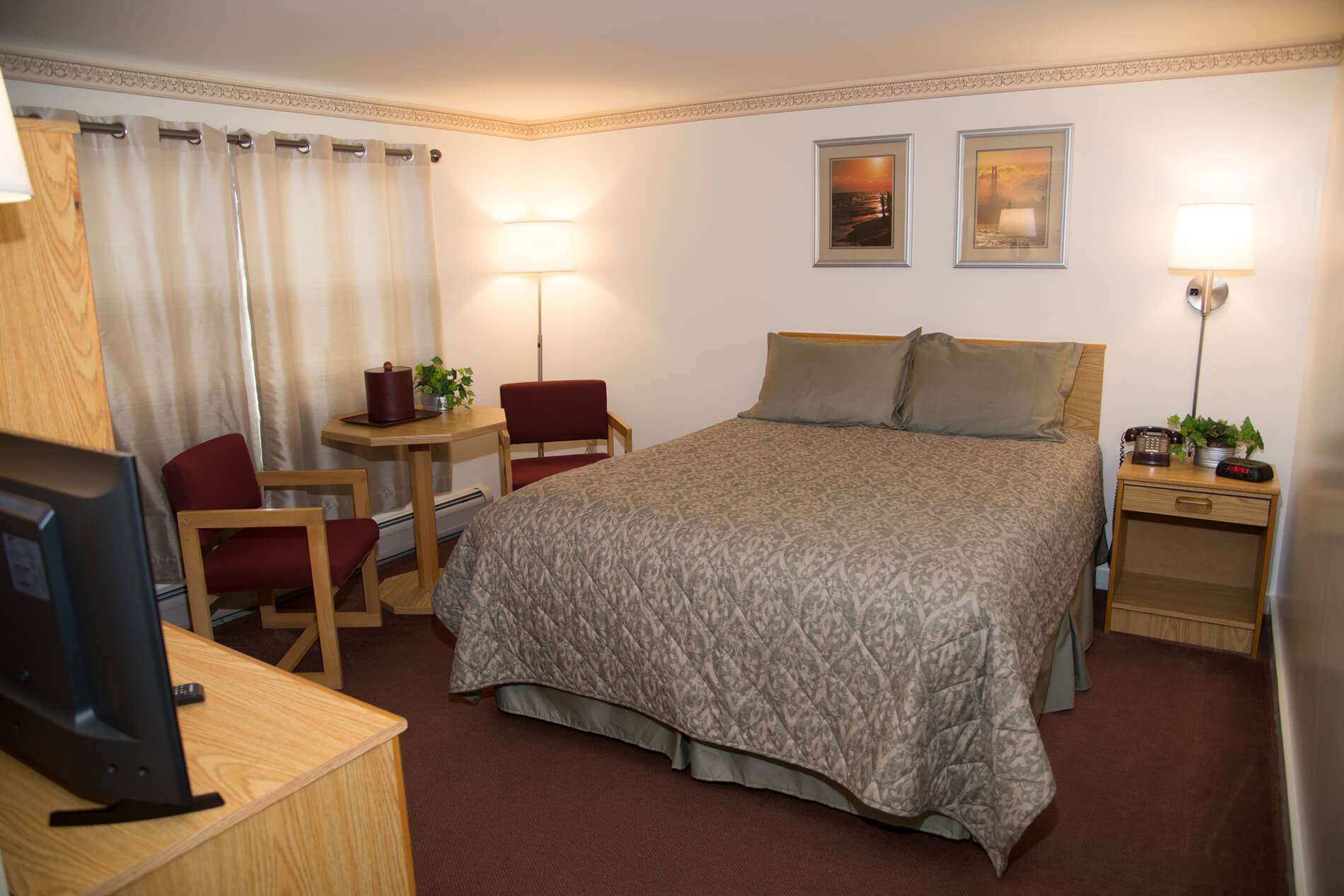Queen size bed with light green bedspread, wooden table and two chairs.