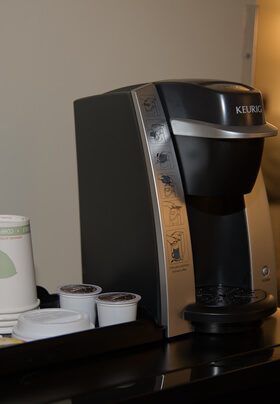 Black coffee making machine with coffee pods, green bedding in background.